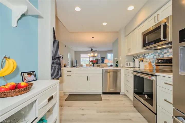 Kitchen featuring kitchen peninsula, appliances with stainless steel finishes, decorative light fixtures, light hardwood / wood-style flooring, and white cabinets