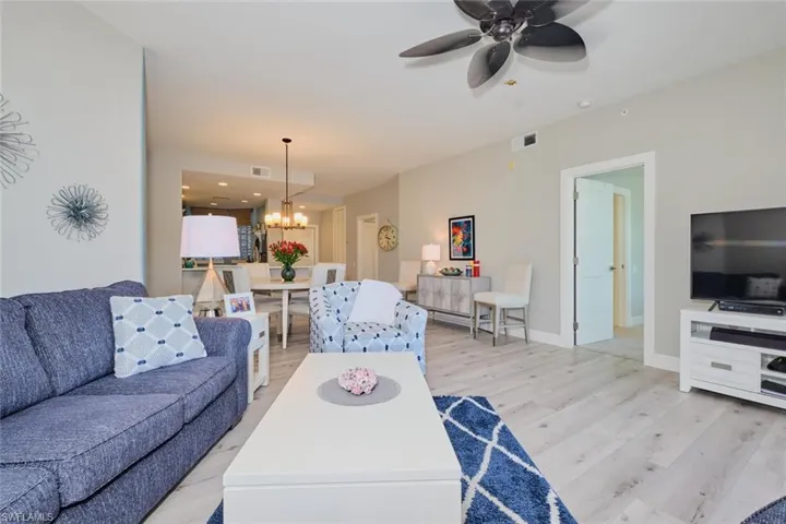 Living room featuring ceiling fan with notable chandelier and light wood-type flooring