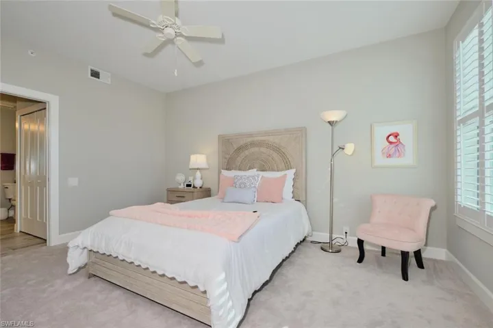 Carpeted bedroom featuring multiple windows and ceiling fan