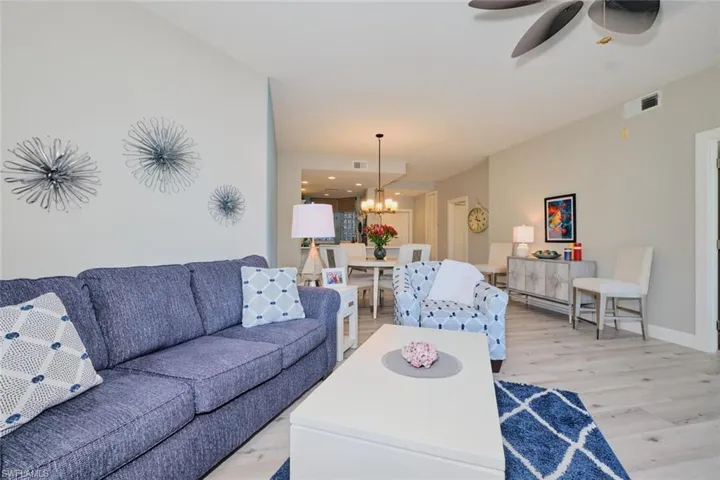 Living room with ceiling fan with notable chandelier and light wood-type flooring