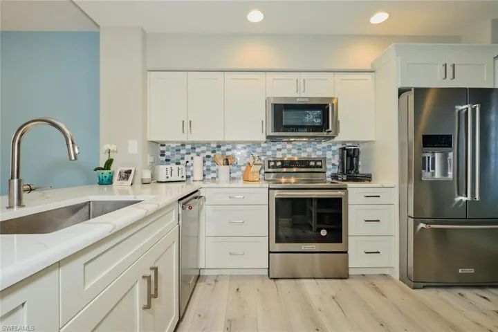 Kitchen with sink, light wood-type flooring, appliances with stainless steel finishes, light stone counters, and white cabinetry