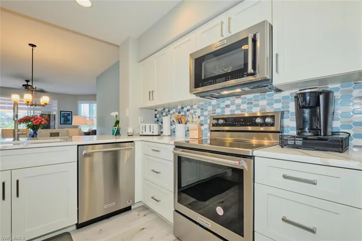Kitchen featuring appliances with stainless steel finishes, tasteful backsplash, a notable chandelier, light hardwood / wood-style floors, and white cabinetry