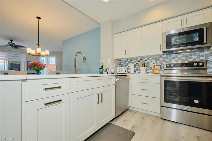 Kitchen featuring pendant lighting, backsplash, white cabinets, light hardwood / wood-style flooring, and stainless steel appliances