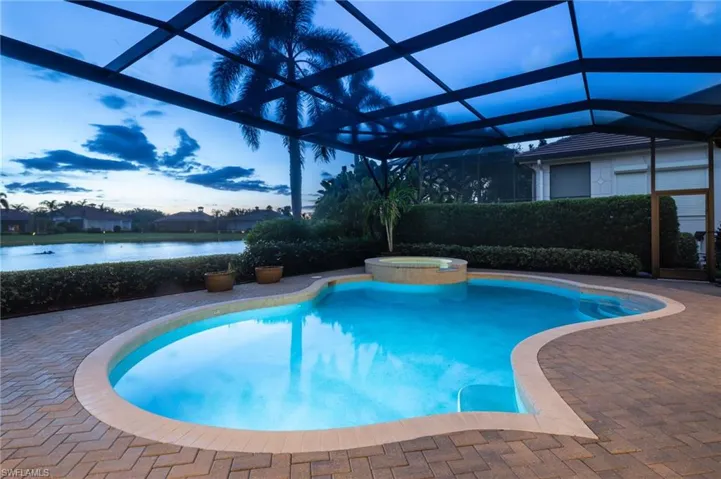 Pool at dusk with a lanai, a pool with connected hot tub, a water view, a patio, and a sunroom