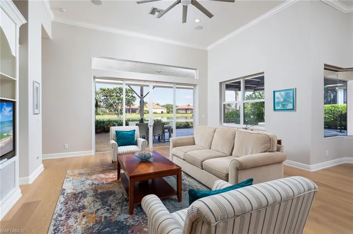 Living area with ornamental molding, light wood finished floors, ceiling fan, recessed lighting, and a towering ceiling