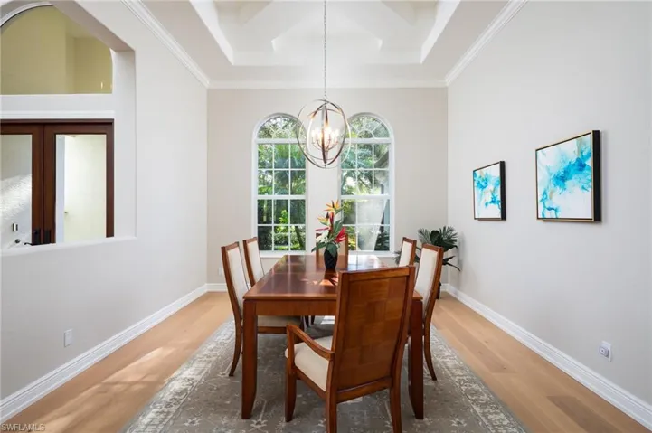 Dining space with wood finished floors, coffered ceiling, a chandelier, ornamental molding, and beam ceiling