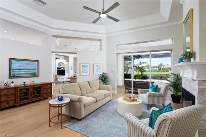 Living area featuring light wood-style floors, a tray ceiling, a fireplace, a ceiling fan, and ornamental molding
