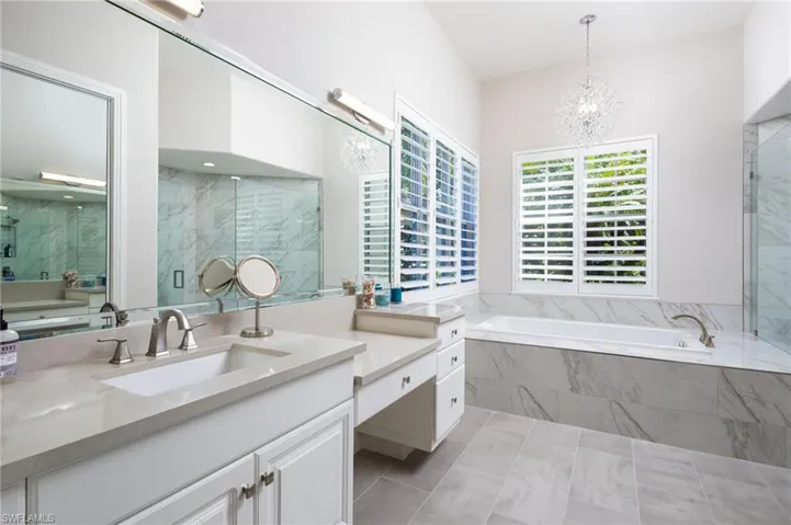 Bathroom featuring a garden tub, a chandelier, a marble finish shower, and vanity