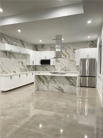 Kitchen with island exhaust hood, white cabinetry, and stainless steel appliances