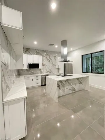 Kitchen with island range hood, stainless steel appliances, sink, a center island, and white cabinets