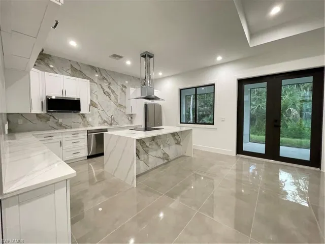 Kitchen with white cabinets, dishwasher, decorative light fixtures, light stone counters, and a kitchen island