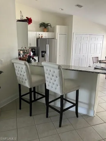 Kitchen featuring a breakfast bar, lofted ceiling, light stone counters, and stainless steel refrigerator with ice dispenser