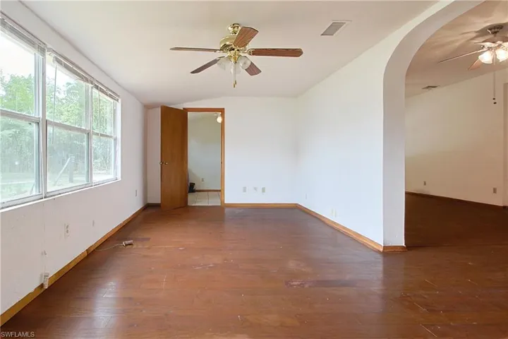 Unfurnished room featuring ceiling fan, arched walkways, dark wood-type flooring, and lofted ceiling