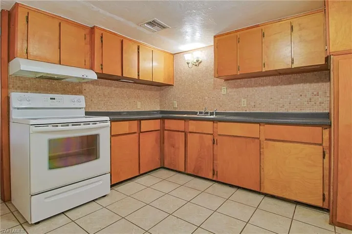 Kitchen with backsplash, white electric range, light tile patterned floors, and a textured ceiling