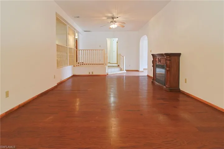 Unfurnished living room featuring dark wood-type flooring, ceiling fan, arched walkways, and a glass covered fireplace
