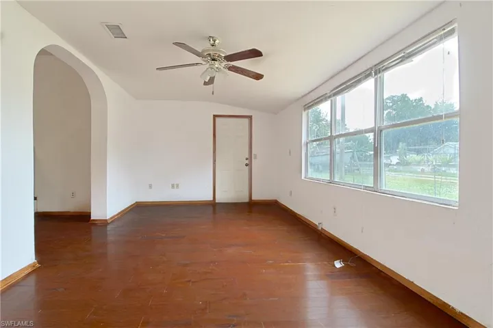 Unfurnished room featuring arched walkways, dark wood-type flooring, vaulted ceiling, and ceiling fan