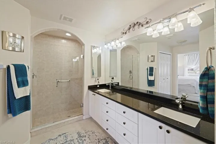 Full bathroom with double vanity, a shower stall, ensuite bathroom, and light tile patterned flooring