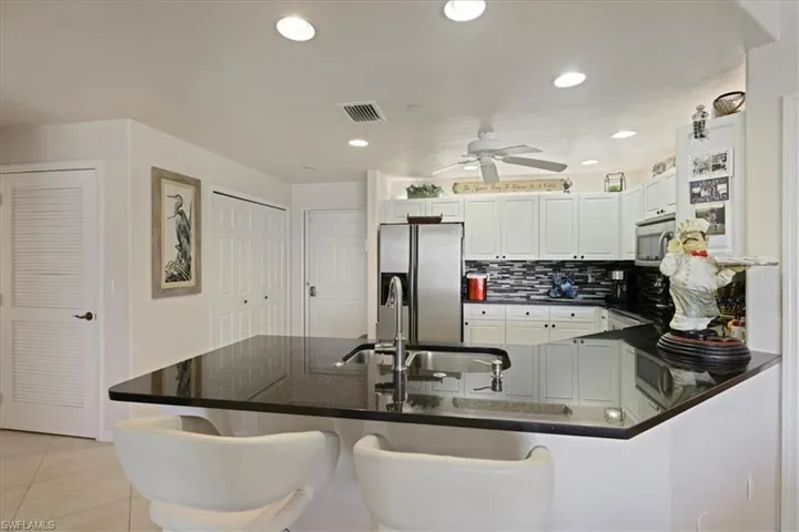 Kitchen featuring stainless steel appliances, a peninsula, a breakfast bar, white cabinetry, and backsplash