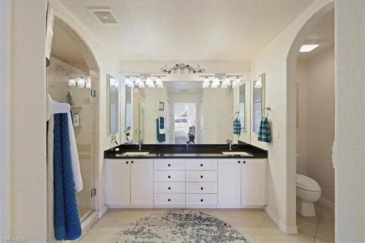 Full bath with a shower stall, a textured ceiling, double vanity, and light tile patterned floors