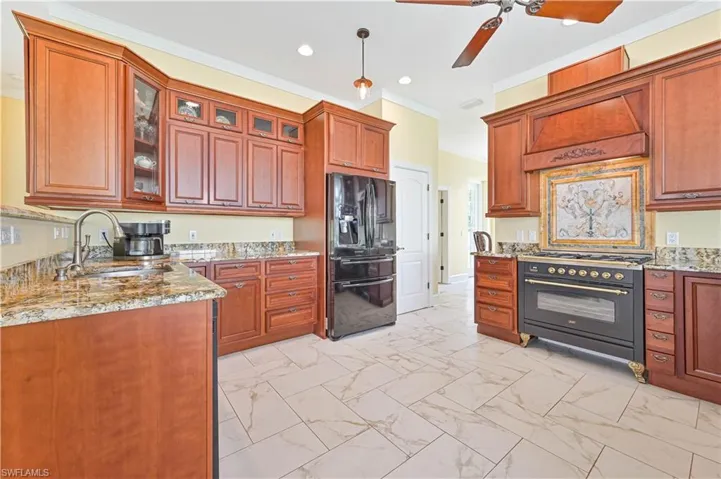 Kitchen featuring black appliances, light stone countertops, sink, and ceiling fan