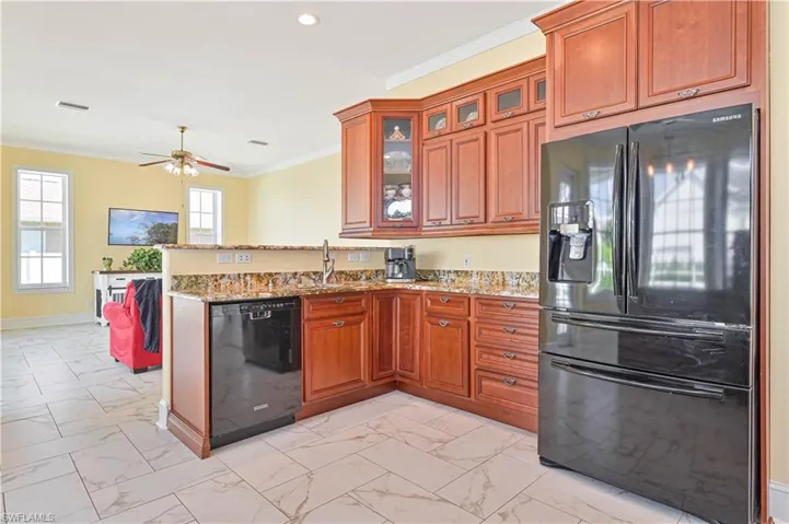 Kitchen featuring kitchen peninsula, black appliances, ceiling fan, and light stone countertops