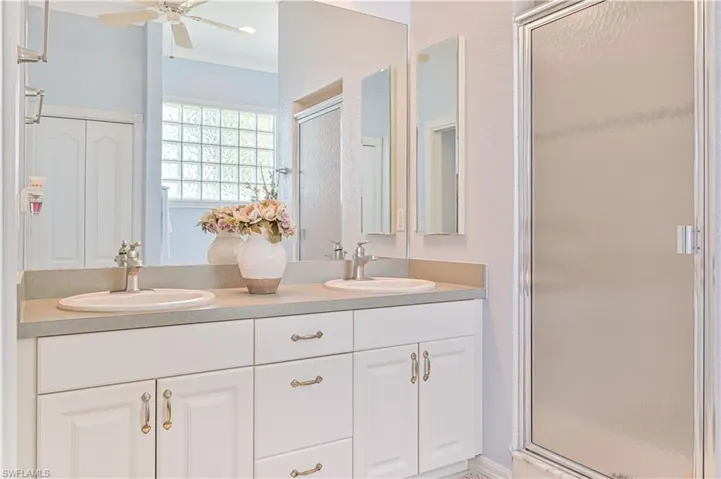 Bathroom featuring ceiling fan, walk in shower, crown molding, and dual bowl vanity