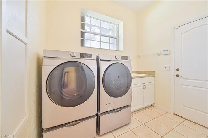 Washroom with light tile patterned flooring, cabinets, and independent washer and dryer