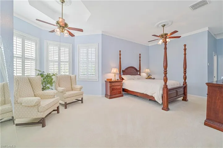 Carpeted bedroom featuring a raised ceiling, crown molding, and ceiling fan