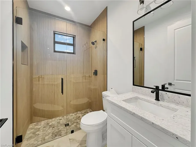 Bathroom featuring tile patterned flooring, a shower with shower door, vanity, and toilet