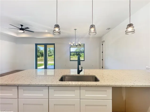 Kitchen featuring sink, white cabinets, light stone counters, and hanging light fixtures