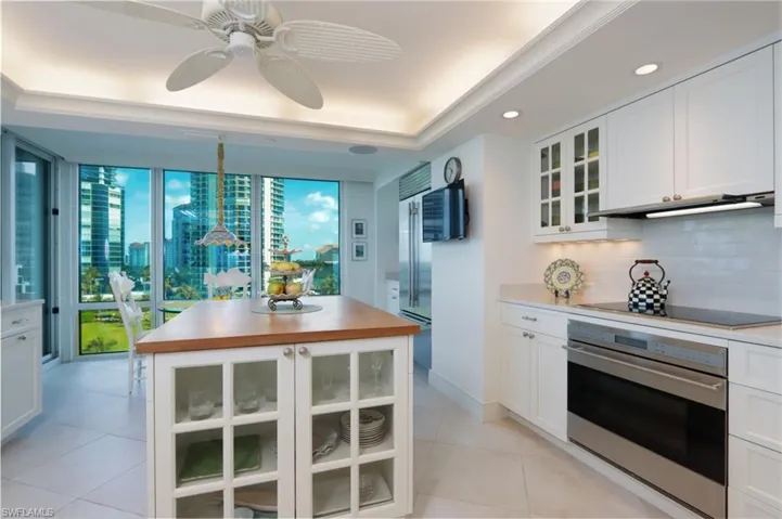 Kitchen featuring glass insert cabinets, stainless steel appliances, white cabinets, a kitchen island, and ceiling fan