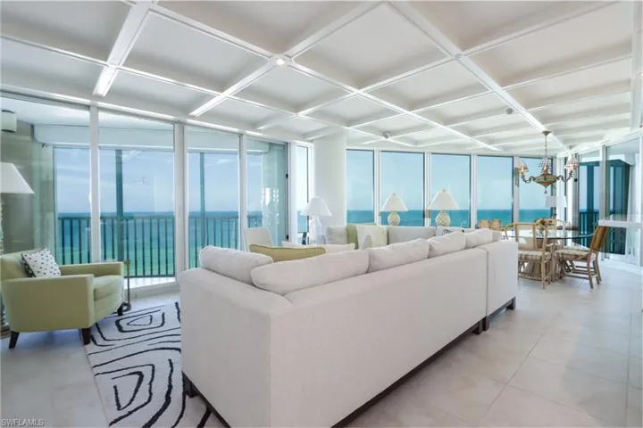 Living area featuring coffered ceiling, expansive windows, a water view, and a chandelier