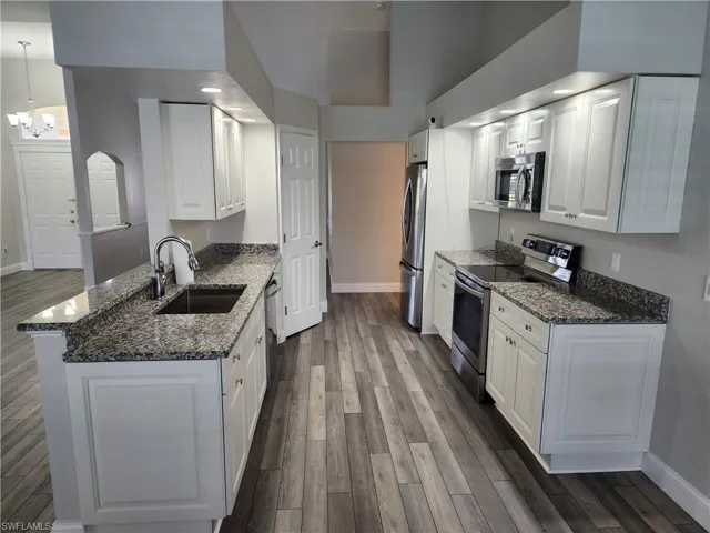 Kitchen featuring medium stone countertops, stainless steel appliances, and vinyl wood-style flooring