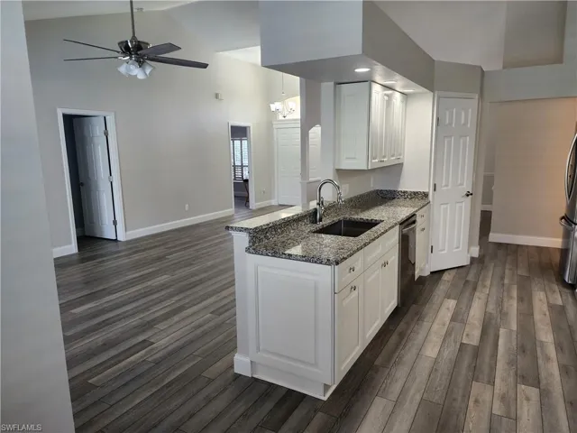 Kitchen with white cabinetry, medium stone counters, vinyl wood-type flooring, ceiling fan, and vaulted ceiling