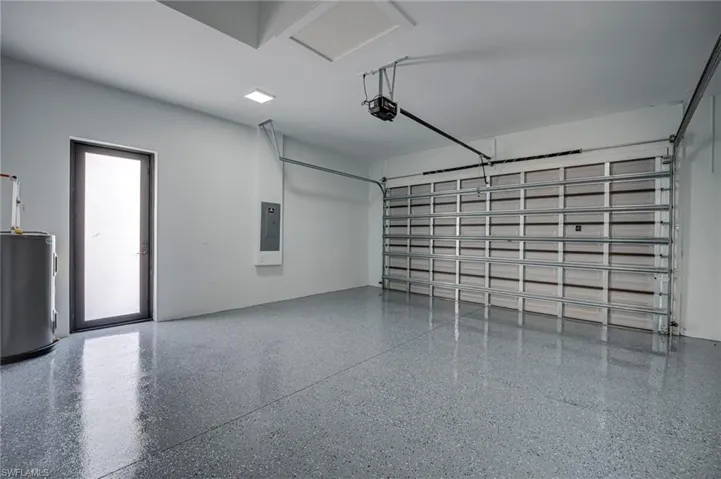 Garage with electric water heater, electric panel, and a garage door opener
