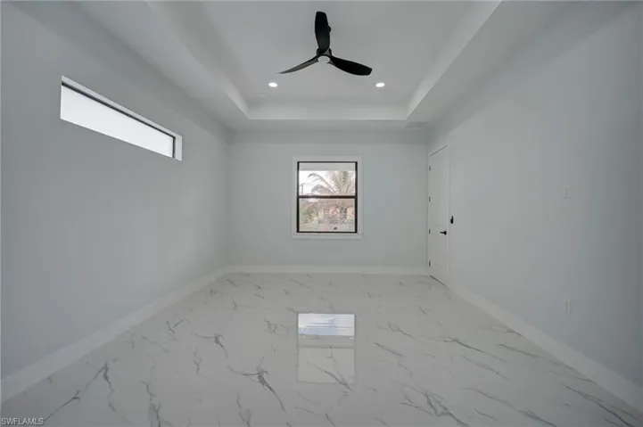 Unfurnished room with light marble finish flooring, a tray ceiling, recessed lighting, and a ceiling fan
