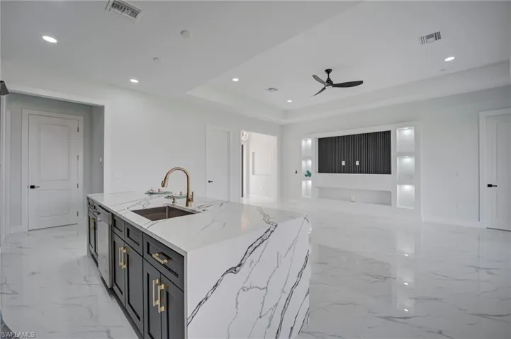 Kitchen with an island with sink, light stone counters, dark cabinets, recessed lighting, and a ceiling fan