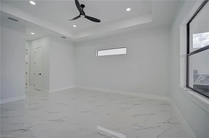 Spare room featuring a tray ceiling, light marble finish floors, a ceiling fan, and recessed lighting