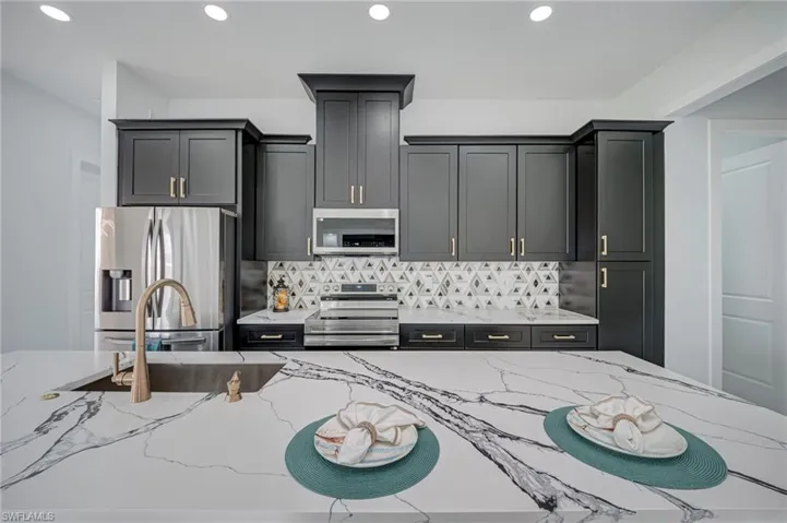 Kitchen with stainless steel appliances, light stone countertops, tasteful backsplash, recessed lighting, and gray cabinetry