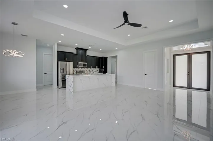 Unfurnished living room featuring a tray ceiling, a ceiling fan, recessed lighting, and french doors