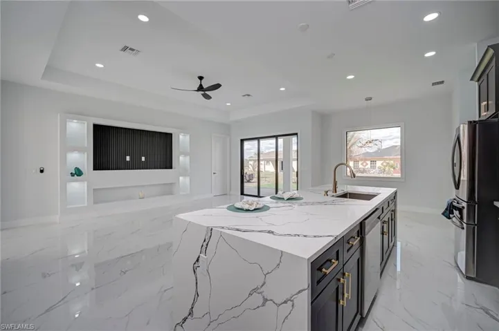 Kitchen featuring a kitchen island with sink, light stone countertops, open floor plan, stainless steel appliances, and light marble finish floors