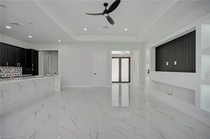 Unfurnished living room featuring ceiling fan, a raised ceiling, recessed lighting, and light marble finish flooring