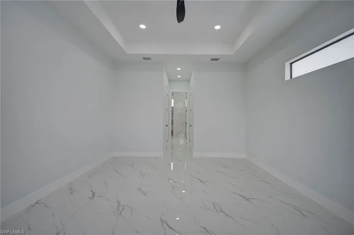 Spare room with recessed lighting, light marble finish floors, a ceiling fan, and a raised ceiling