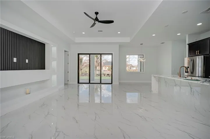 Unfurnished living room with ceiling fan, a raised ceiling, light marble finish flooring, and recessed lighting