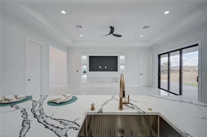 Kitchen featuring light stone countertops, recessed lighting, ceiling fan, open floor plan, and a tray ceiling