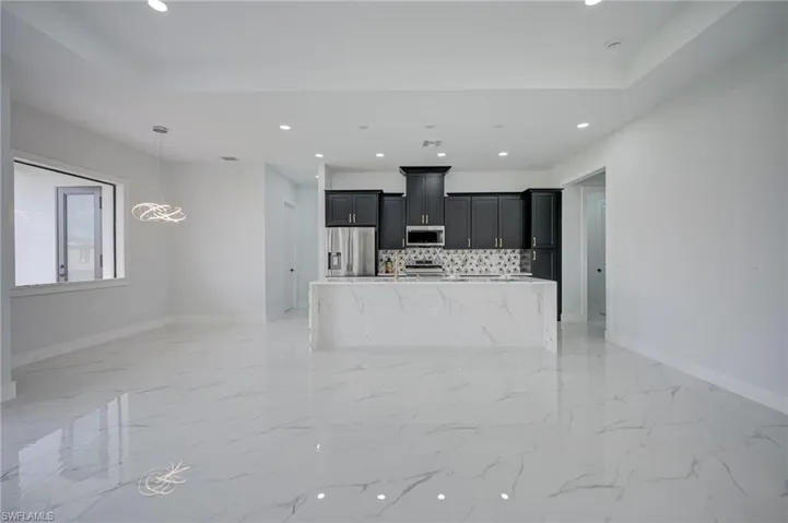 Kitchen with stainless steel appliances, a kitchen island with sink, dark cabinets, and open floor plan