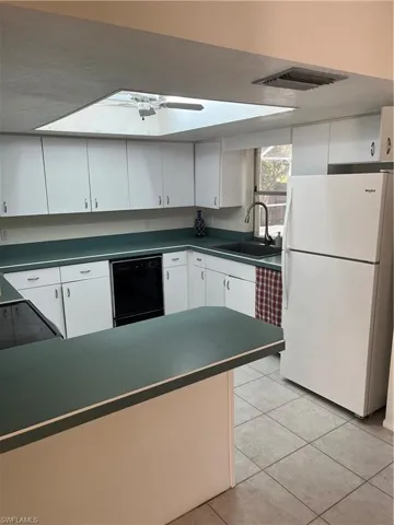 Kitchen with refrigerator, dark countertops, visible vents, a sink, and dishwasher
