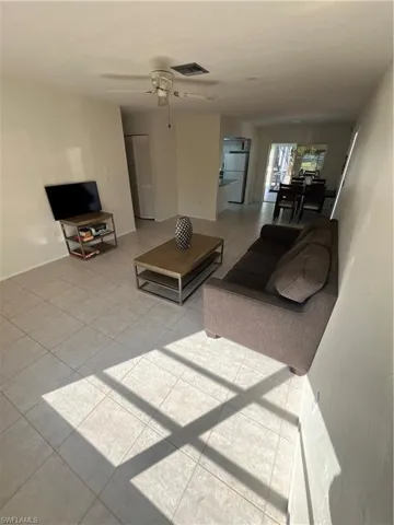 Living area with light tile patterned floors, baseboards, visible vents, and a ceiling fan