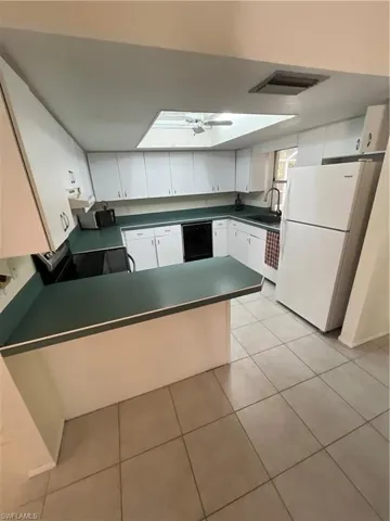 Kitchen featuring refrigerator, dark countertops, stove, a sink, and a peninsula