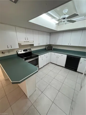 Kitchen featuring dishwashing machine, dark countertops, wall chimney exhaust hood, and stove